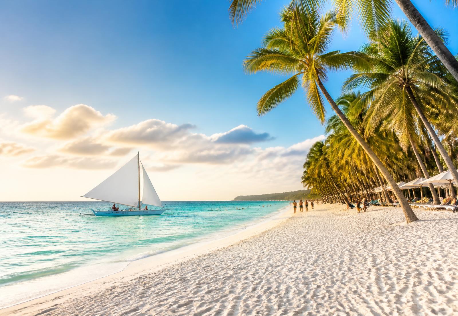 White sand beach in Boracay with a paraw sailboat, turquoise water and palm trees